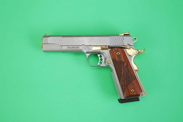 steel gun or pistol inlaid with wood and gold isolated on a green background. weapon concept. protection and violence.