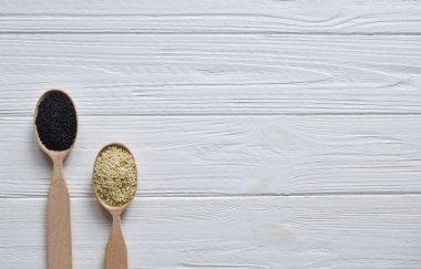 Beyaz ahşap zemin üzerinde tahta kaşıklar içinde siyah ve Beyaz Susam. Üstten görünüm. Kopya alanı