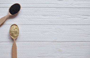 Beyaz ahşap zemin üzerinde tahta kaşıklar içinde siyah ve Beyaz Susam. Üstten görünüm. Kopya alanı