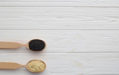 Beyaz ahşap zemin üzerinde tahta kaşıklar içinde siyah ve Beyaz Susam. Üstten görünüm. Kopya alanı