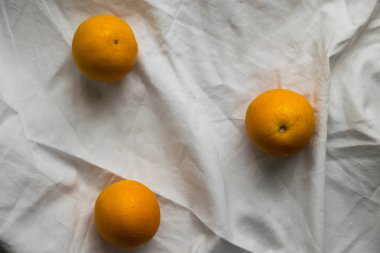 Beyaz kumaş arka plan üzerinde üç portakal. Üstten görünüm