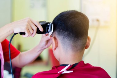 Kuaför Salonu. Kuaför saç modeli saç kesme makinesi ve beyaz tarak Asyalı bir çocuk yapar. Çocuklar için şık saç kesimi.