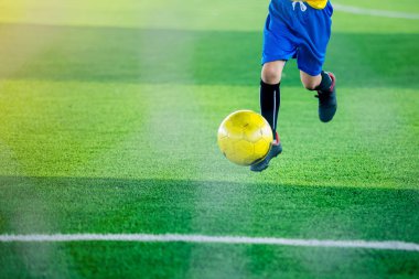 Çocuk futbolcu yeşil yapay çim üzerinde sarı topu vur. Arka planı için.