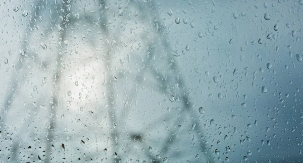 Water droplet on windshield with blurry electric transmission tower background.