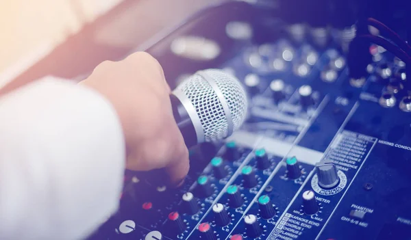 Microphone in hand and adjust an audio mixer controller in the control room, Sound mixer control for live music and studio equipment, Quality audio system for professionals, music equipment concept.