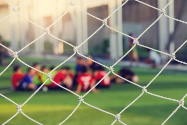 Beyaz kafes amacı ile koç ile yeşil yapay çim üzerinde oturan bulanık genç çocuk futbol oyuncuları.