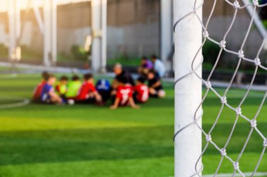 Beyaz kafes amacı ile koç ile yeşil yapay çim üzerinde oturan bulanık genç çocuk futbol oyuncuları.