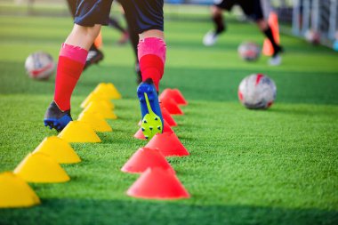 Çocuk futbolcu koşu ve futbol eğitim için işaretleyici arasında atlamak.