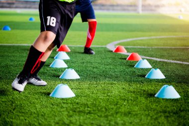 Futbolcu koşu ve futbol eğitim için yeşil suni çim üzerinde koni işaretleri arasında atlamak. Futbol ya da futbol Akademisi.