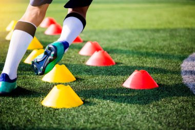 Futbolcu koşu ve futbol eğitim için yeşil suni çim üzerinde koni işaretleri arasında atlamak. Futbol ya da futbol Akademisi.