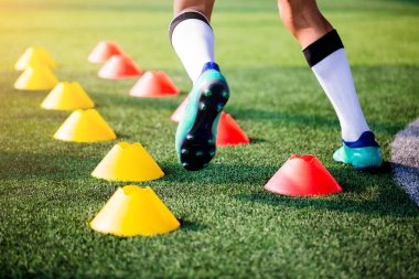 Futbolcu koşu ve futbol eğitim için yeşil suni çim üzerinde koni işaretleri arasında atlamak. Futbol ya da futbol Akademisi.