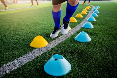 Futbolcu koşu ve futbol eğitim için yeşil suni çim üzerinde koni işaretleri arasında atlamak. Futbol ya da futbol Akademisi.