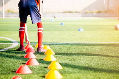 Futbolcu koşu ve futbol eğitim için yeşil suni çim üzerinde koni işaretleri arasında atlamak. Futbol ya da futbol Akademisi.