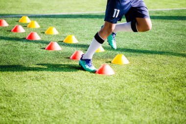 Futbolcu koşu ve futbol eğitim için yeşil suni çim üzerinde koni işaretleri arasında atlamak. Futbol ya da futbol Akademisi.