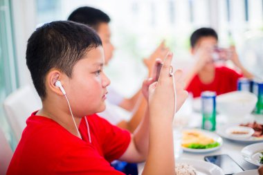 Asyalı çocuk oyun smartphone ile kulaklık ve arkadaşları için oyun ve eğlence restoranda yemek masasında