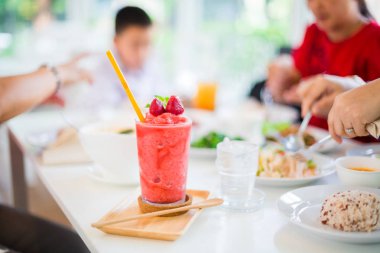 Çilek suyu bulanık kadınlarla Restoran beyaz masaya sallamak ve çocuk yemek yeme