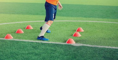 Futbolcu koşu ve futbol eğitim için yeşil suni çim üzerinde koni işaretleri arasında atlamak. Futbol ya da futbol Akademisi.