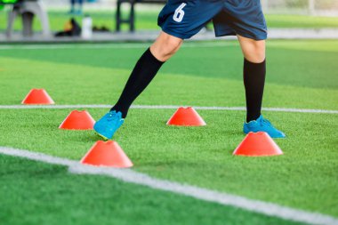 Futbolcu koşu ve futbol eğitim için yeşil suni çim üzerinde koni işaretleri arasında atlamak. Futbol ya da futbol Akademisi.