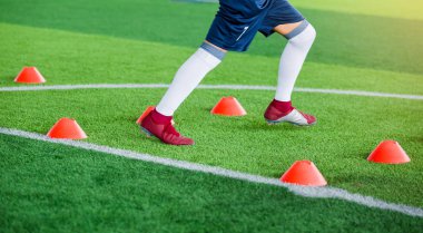 Futbolcu koşu ve futbol eğitim için yeşil suni çim üzerinde koni işaretleri arasında atlamak. Futbol ya da futbol Akademisi.