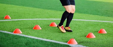 Futbolcu koşu ve futbol eğitim için yeşil suni çim üzerinde koni işaretleri arasında atlamak. Futbol ya da futbol Akademisi.