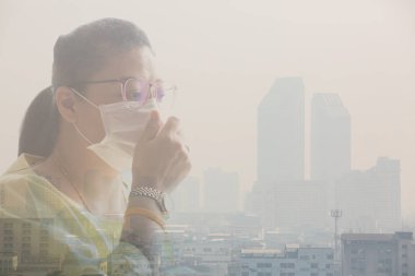 Woman wearing face mask because of air pollution in the Bangkok. Woman wearing face mask with background of Office building under smog in Bangkok, Thailand. Smog is a kind of air pollution. Bangkok City in the air pollution.