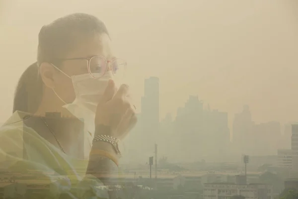 Woman wearing face mask because of air pollution in the Bangkok. Woman wearing face mask with background of Office building under smog in Din Daeng District, Bangkok Thailand. Smog is a kind of air pollution. Bangkok City in the air pollution.