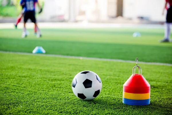 Soccer ball and cone marker on green artificial turf with blurry of soccer player training. Soccer academy