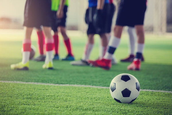 soccer ball on green artificial turf with blurry soccer players standing before training and start game.