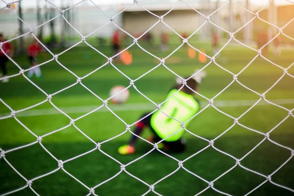 Mesh of goal with blurry of soccer goalkeeper and soccer players. Soccer ball training in academy.
