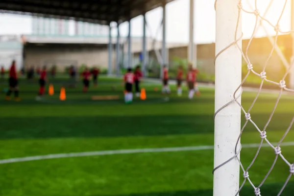 White goalposts and mesh of goal with blurry football players. football academy.