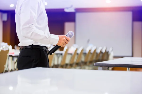 The speaker held the microphone in his hand with blurry conferen