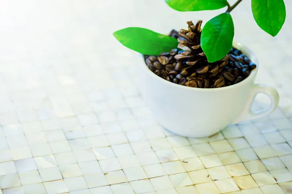 Granos de café y hojas verdes en una taza blanca sobre una mesa — Foto de Stock