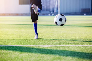Asyalı çocuk futbolcu yapay çim üzerinde sıçrama topu ateş