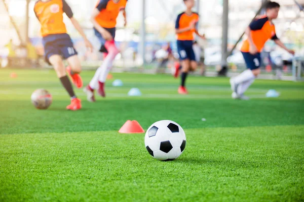 Pallone da calcio e coni marcatori su erba artificiale verde con sfocatura — Foto Stock