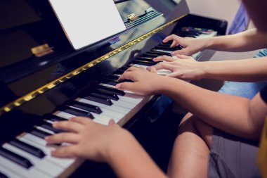 Bir çocuk tablette kadın öğretmen ve müzik gösterimi ile piyano öğreniyor, piyano çalan iki kişiden dört el, Müzik öğrenmek için müzik aleti, Müzik öğrenme konsepti, Seçici odak.
