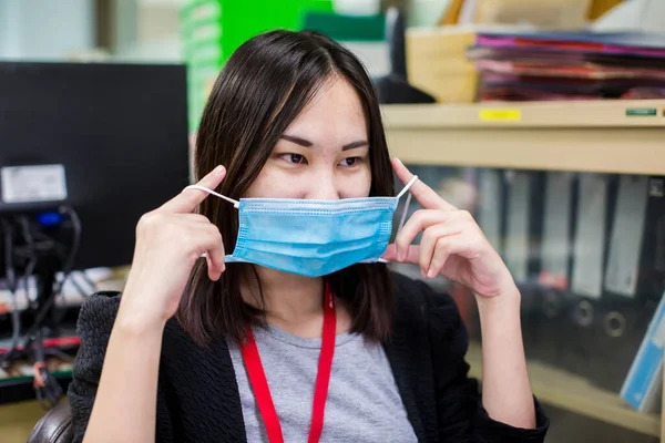 Asian woman employee is wearing medical facial mask working alone as of social distancing policy in the business office during new normal change after coronavirus Covid-19 outbreak pandemic situation.