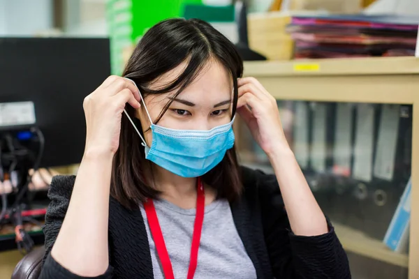 Asian woman employee is wearing medical facial mask working alone as of social distancing policy in the business office during new normal change after coronavirus Covid-19 outbreak pandemic situation.