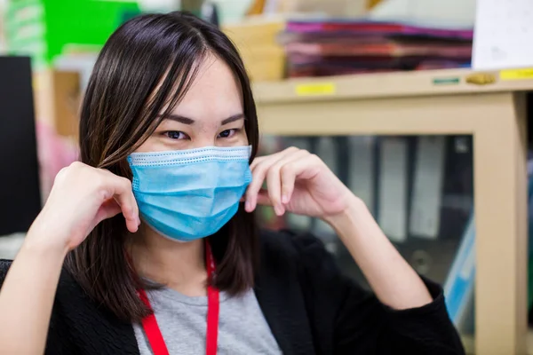 Asian woman employee is wearing medical facial mask working alone as of social distancing policy in the business office during new normal change after coronavirus Covid-19 outbreak pandemic situation.