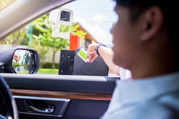 Man driver stop car and use key card to open the door for safety with blurry CCTV camera. Driver hold card to scan at RFID card reader station for open the car park door. security system for parking.