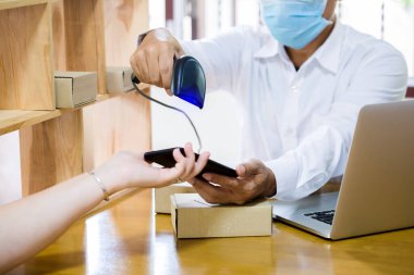 Postanede Coronavirus Covid-19 'u korumak için maske takan personel. Müşteri bilgilerini okumak için akıllı telefondaki barkodu taramak için barkod okuyucu kullanmaya çalışan personel.