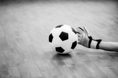 Futsal kalecinin elindeki topun siyah ve beyaz görüntüsü ahşap futsal zeminde. Kapalı spor salonu. Futbolcu, top, spor geçmişi. Gençler Futsal Ligi.