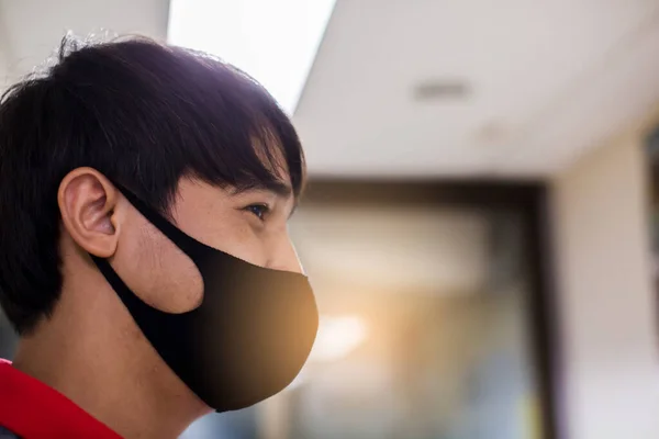 Asian man wears a black face mask that protects against the spread of Coronavirus disease. Close up of a young man wearing a surgical mask on his face against Covid-19.