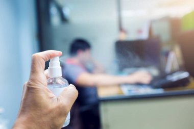 El, ofiste çalışan bulanık işadamlarıyla alkol püskürtüyor. Covid 19 'u korumak için ofisteki temizlik kavramı.