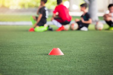 Kırmızı koni işaretleyicisi için seçici odak noktası yeşil suni sahada futbol eğitim ekipmanları ve bulanık çocuk oyuncuların eğitim geçmişi. Futbol akademisinin eğitim sınıfı için malzeme..