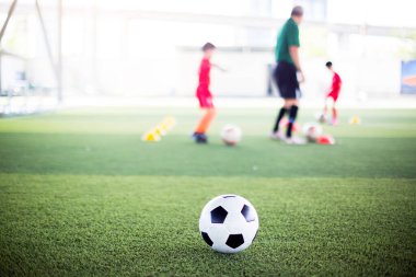 Yeşil suni sahada futbol topu ve bulanık çocuk futbol takımı eğitimi. Bulanık futbolcu çocuk futbol akademisinde futbol ekipmanıyla işaret konileri arasında koşuyor..