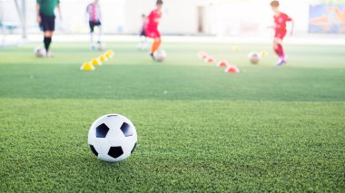Yeşil suni sahada futbol topu ve bulanık çocuk futbol takımı eğitimi. Bulanık futbolcu çocuk futbol akademisinde futbol ekipmanıyla işaret konileri arasında koşuyor..