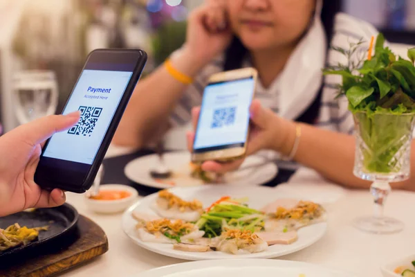 Selective focus to smartphone in hand to scan QR code on tag with blurry food, dessert and customers in restaurant to accepted generate digital pay without money. Qr code payment concept.