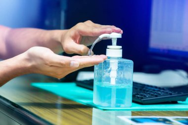 Coronavirus Covid-19 'un bulaşmasını önlemek için alkol dezenfektanı ile el yıkamak. Ofisteki bulanık bilgisayarla el yıkama. Covid 19 'u korumak için ofisteki temizlik kavramı.