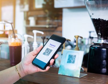 Müşteri akıllı telefon kullanarak kahve dükkanındaki bulanık kahve değirmeniyle QR kod ödeme etiketini tarayıp para almadan dijital ödeme yapmayı kabul ediyor. Qr kod ödeme kavramı.