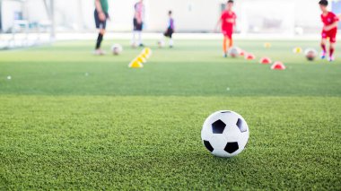 Yeşil suni sahada futbol topu ve bulanık çocuk futbol takımı eğitimi. Bulanık futbolcu çocuk futbol akademisinde futbol ekipmanıyla işaret konileri arasında koşuyor..